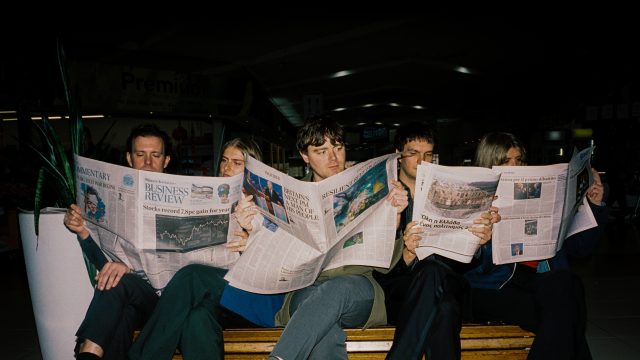 Aussie rock band Delivery sits in a row, reading newspapers